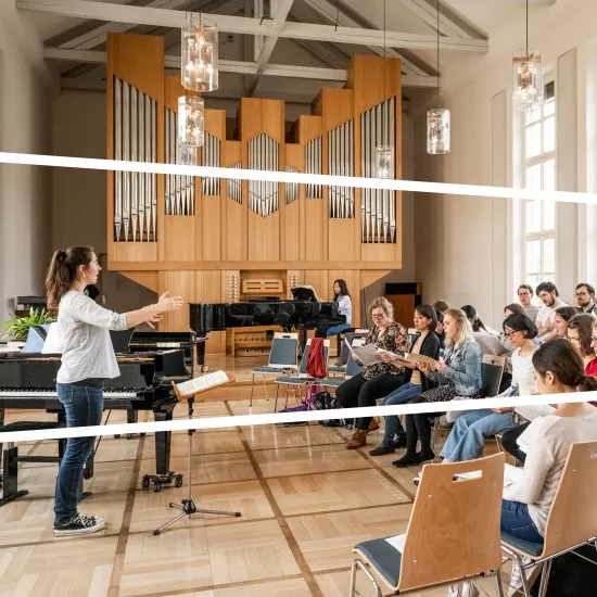 Kirchenchor bei der Probe mit Chorleiterin in einem hellen Raum mit Orgel und Flügel