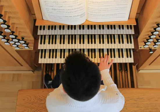 Vogelperspektive auf einen dunkelhaarigen Mann, der die Orgel spielt. 