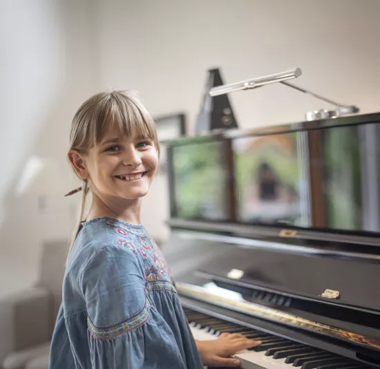 Ein Mädchen am Klavier lächelt in die Kamera