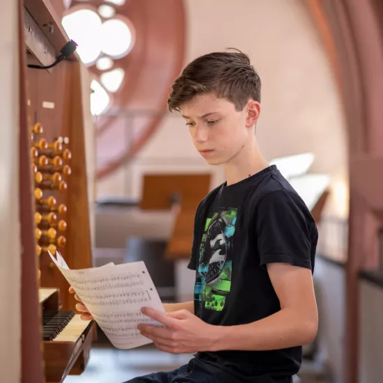 Junge mit Notenblatt vor Orgel