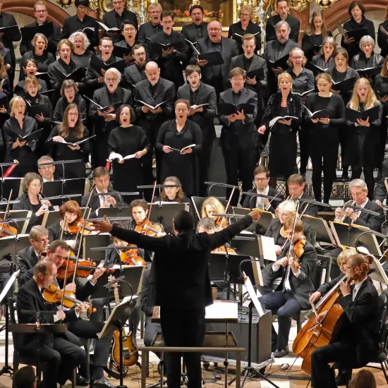 Ein Chor und Orchester in schwarz gekleidet mit Dirigent