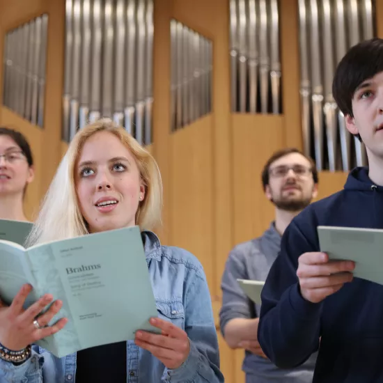 4 Personen mit Gesangsbüchern vor einer Orgel